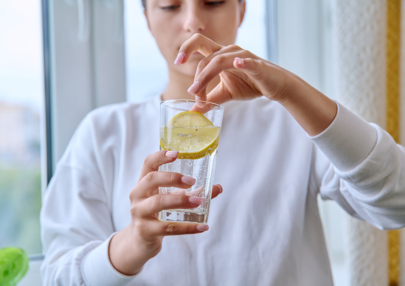 Close-up of glass of water with lemon in hands of young female. Healthy drink, refreshing vitamin beverage