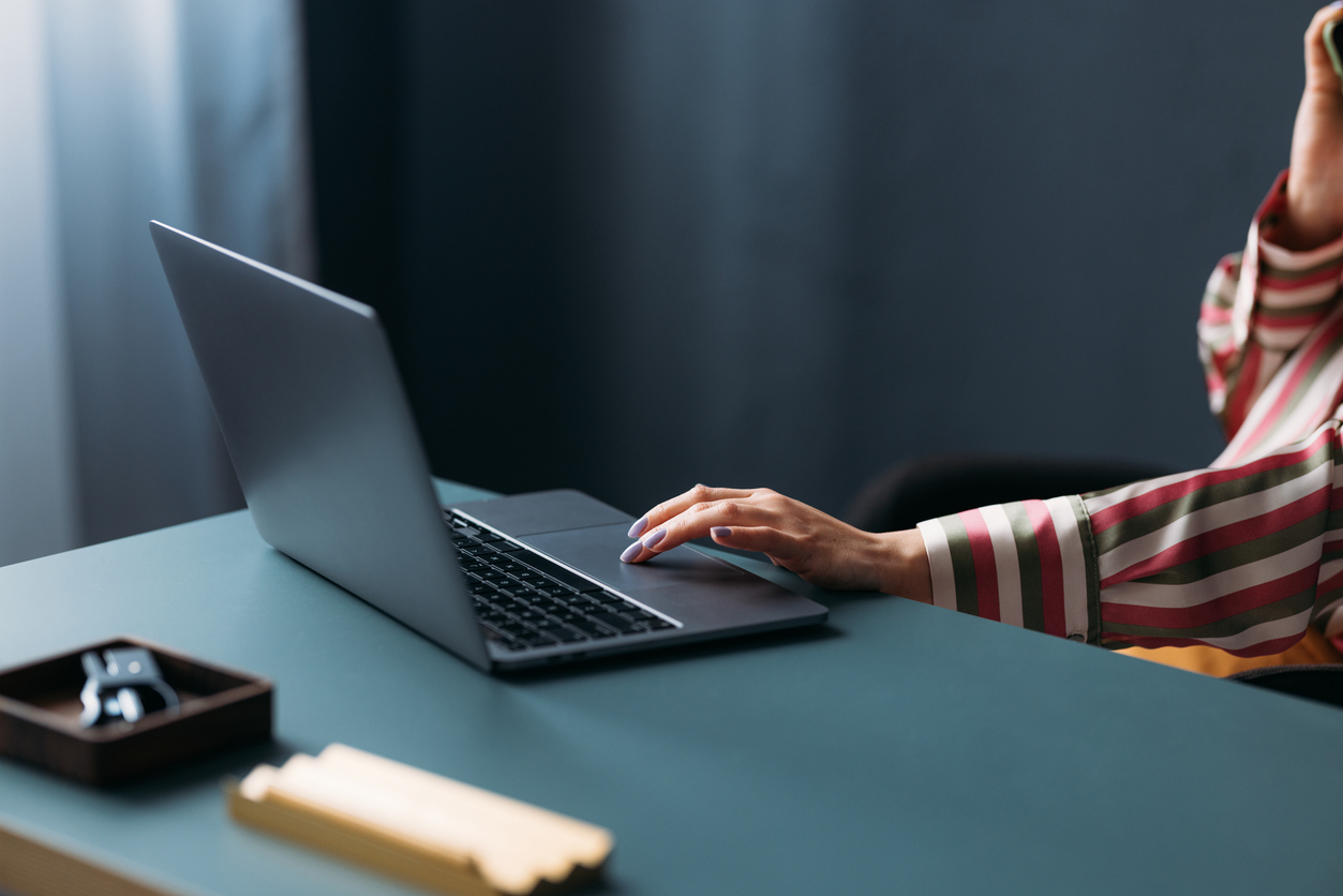 Close-up of a woman's hand using a laptop on a clean desk with minimalist style in an office environment.
