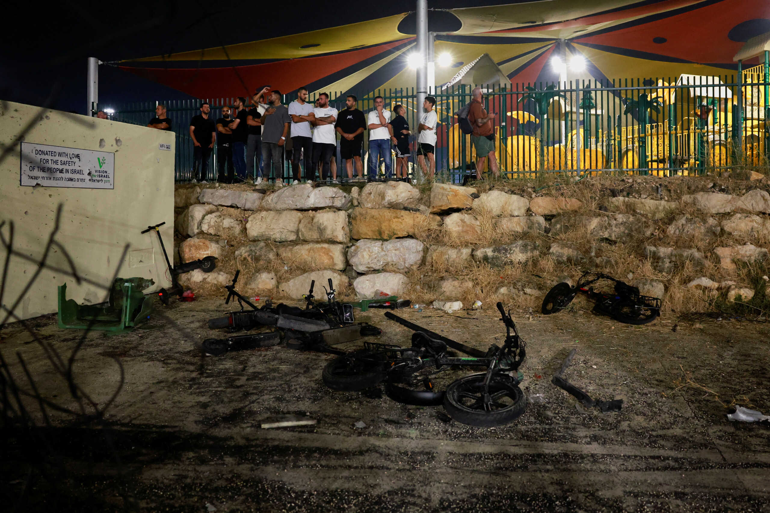 People stand as Israeli officials respond after rockets were launched across Lebanon's border with Israel which, according to Israel's ambulance services, people were killed, at a soccer pitch in Majdal Shams, a Druze village in the Israeli-occupied Golan Heights, July 27, 2024. REUTERS