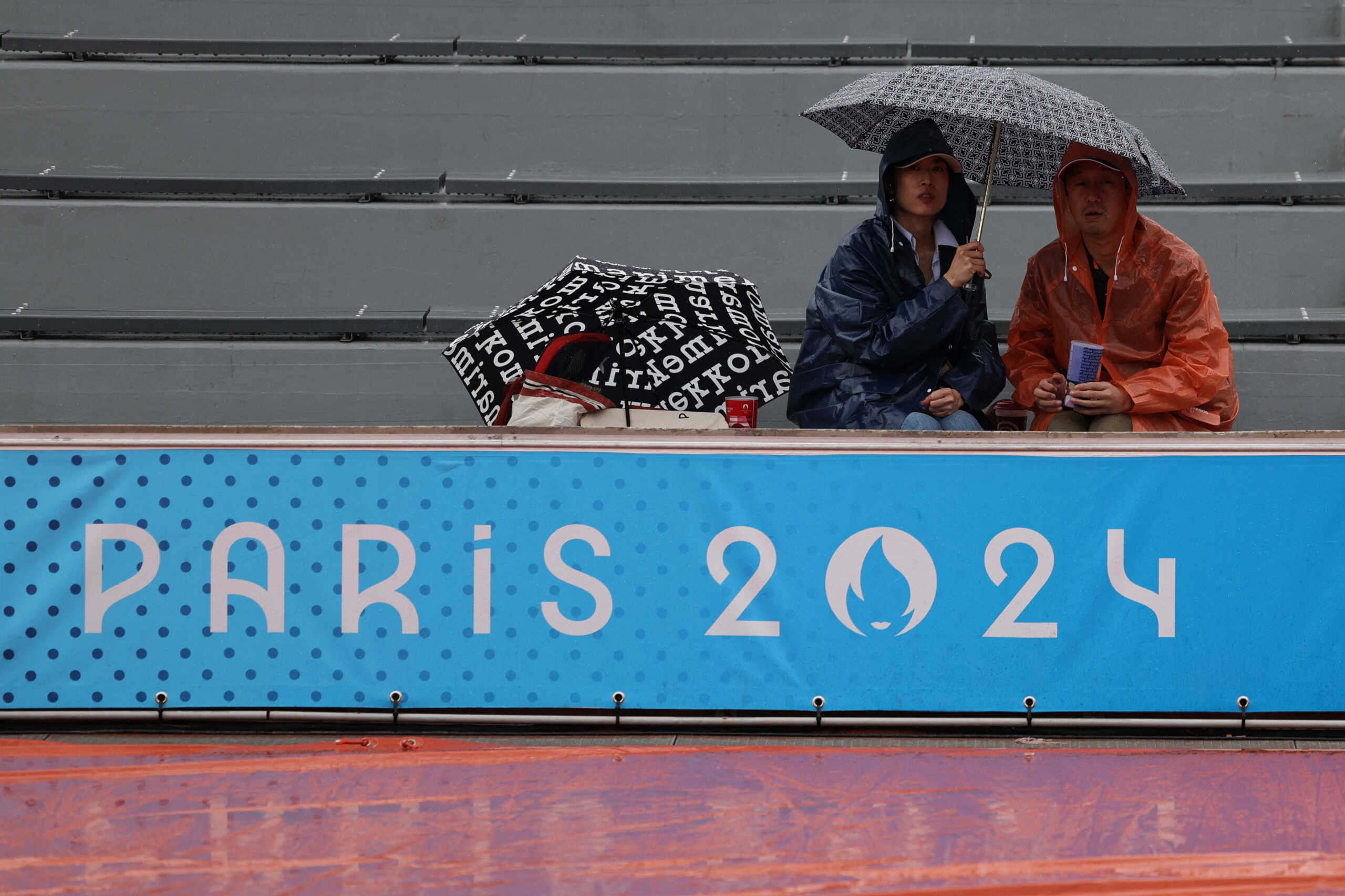 Paris 2024 Olympics - Tennis - Men's Singles First Round - Roland-Garros Stadium, Paris, France - July 27, 2024. Spectators cover themselves from the rain as match is delayed due to wet weather conditions. REUTERS