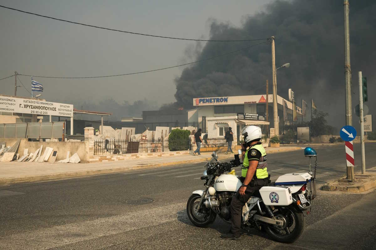 A police officer speaks on his radio in front of rising smoke, as a wildfire burns in Chalandri, Greece, August 12, 2024. REUTERS