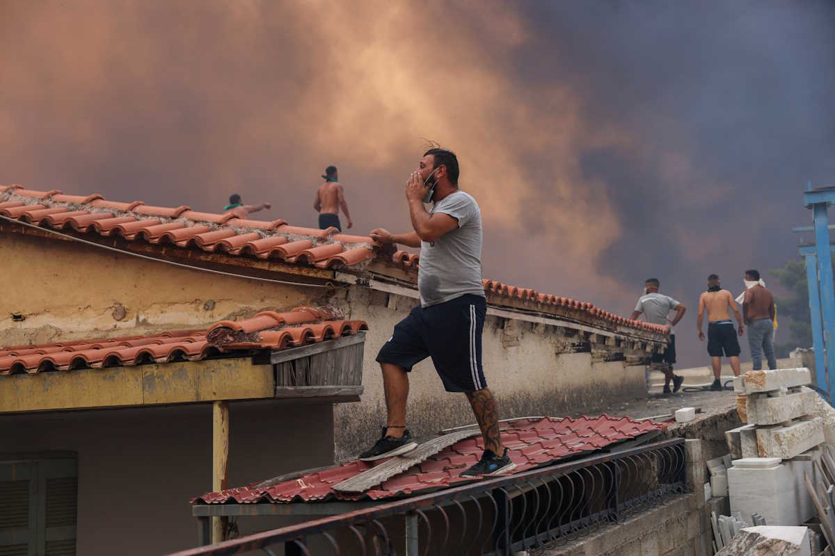 People stand on the roof of a building as smoke rises from a wildfire burning in Vrilissia, near Athens, Greece, August 12, 2024. REUTERS