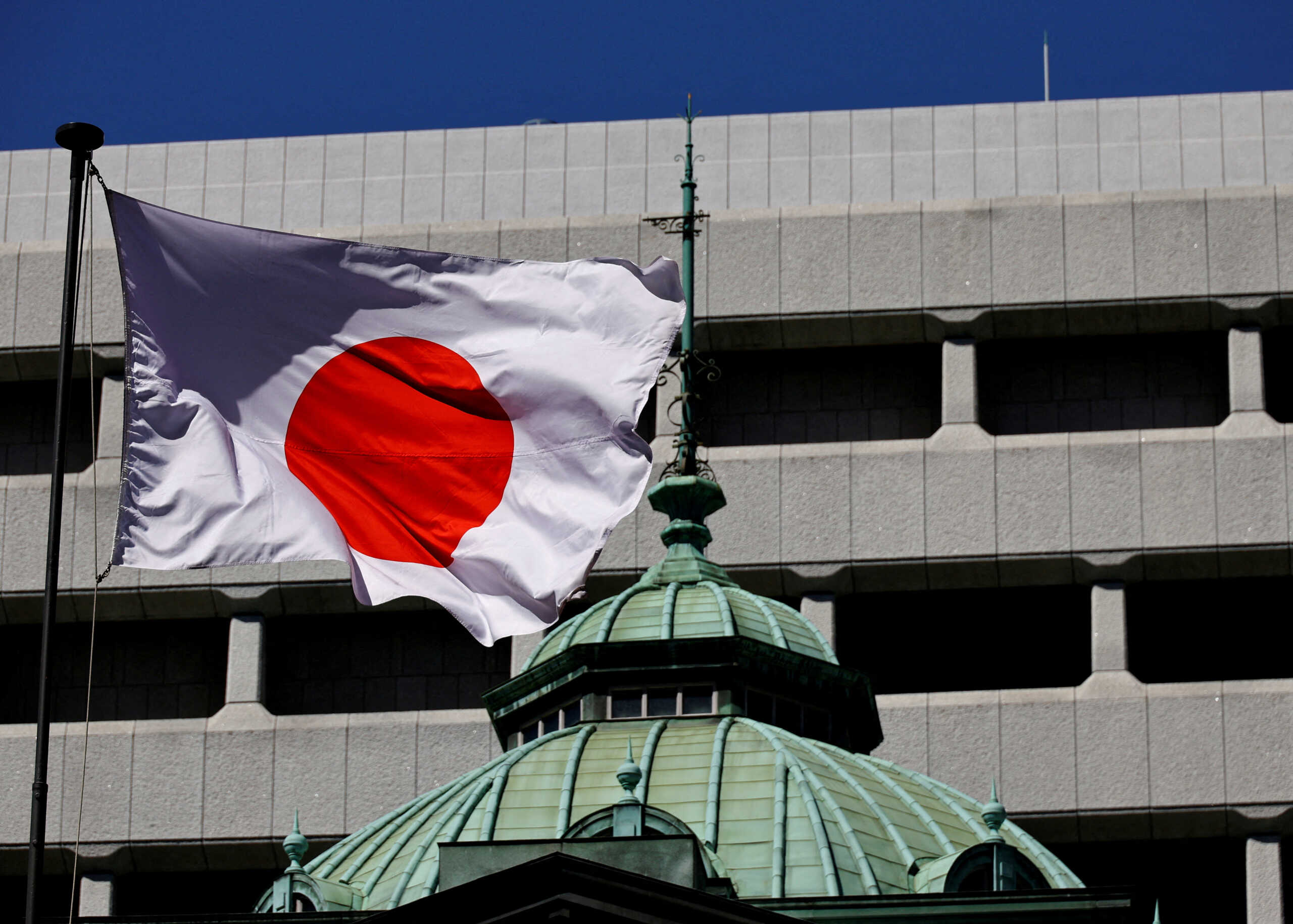 FILE PHOTO: The Japanese national flag waves at the Bank of Japan building in Tokyo, Japan March 18, 2024. REUTERS