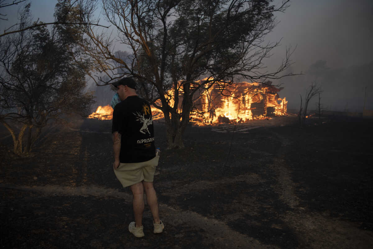 A man reacts as a house is on fire in Varnava village during a wildfire, north of Athens, Greece, Sunday, Aug. 11, 2024, with many regions of the country on high alert due to high temperatures and wind speeds. (AP Photo