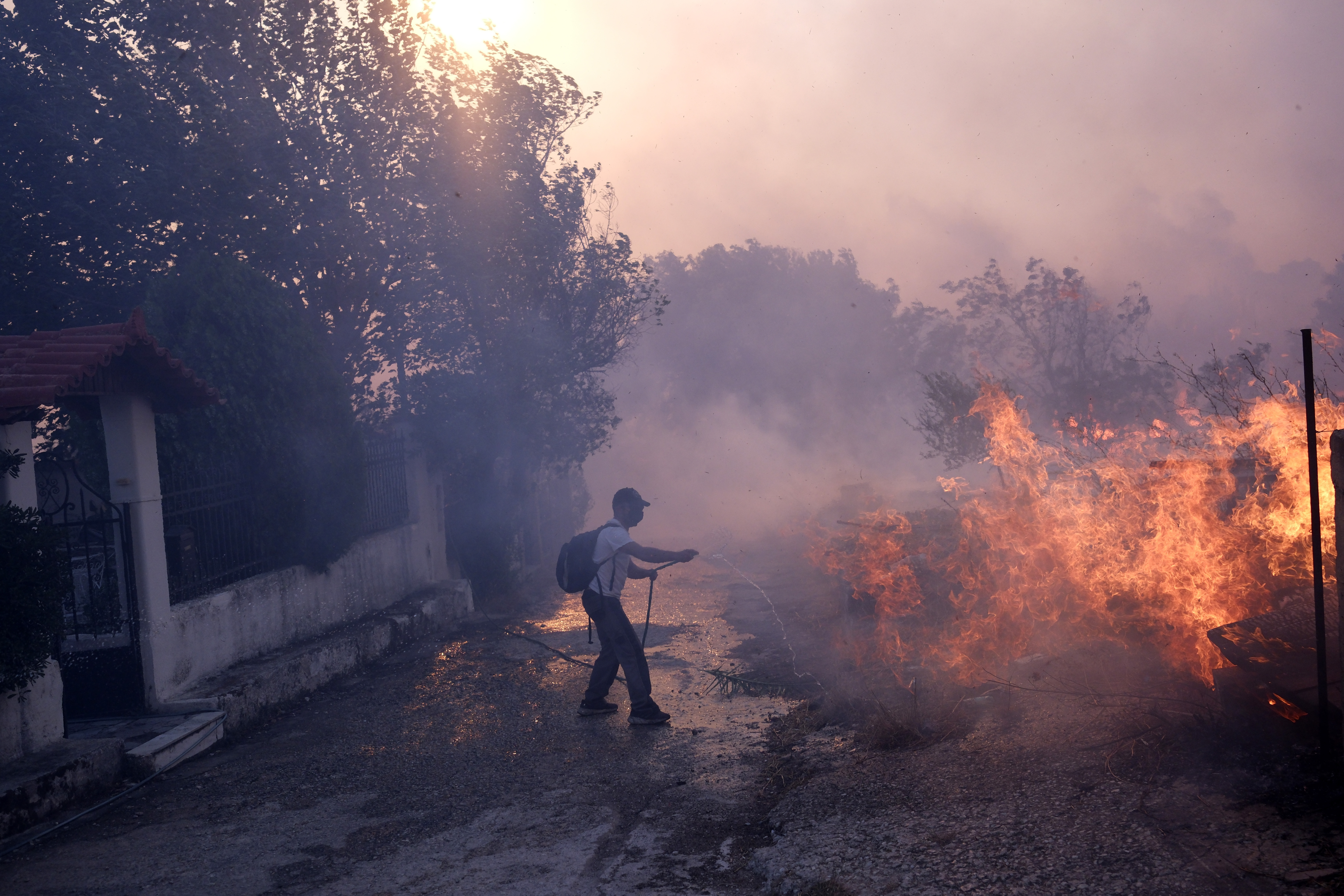 A man tries to extinguish the flames near a house during a fire in northern Athens, Monday, Aug. 12, 2024, as hundreds of firefighters tackle a major wildfire raging out of control on fringes of Greek capital. (AP Photo