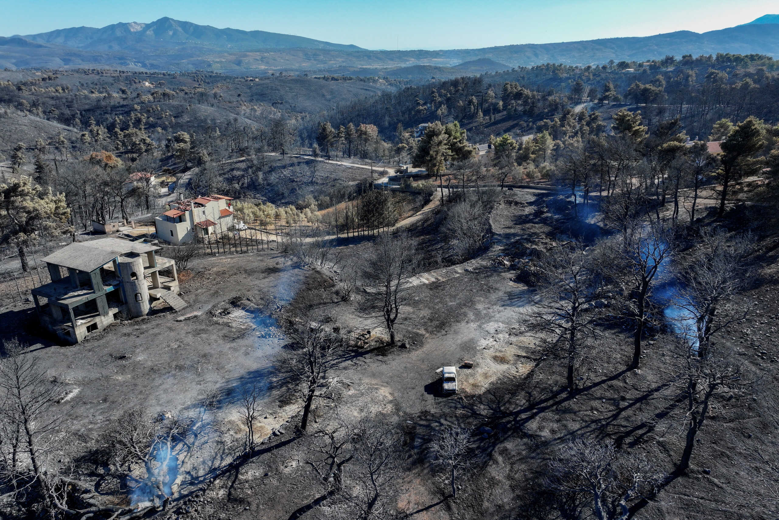 A drone view shows destroyed houses and a destroyed car in a charred forest area following a wildfire, in the village of Varnavas, Greece, August 13, 2024. REUTERS