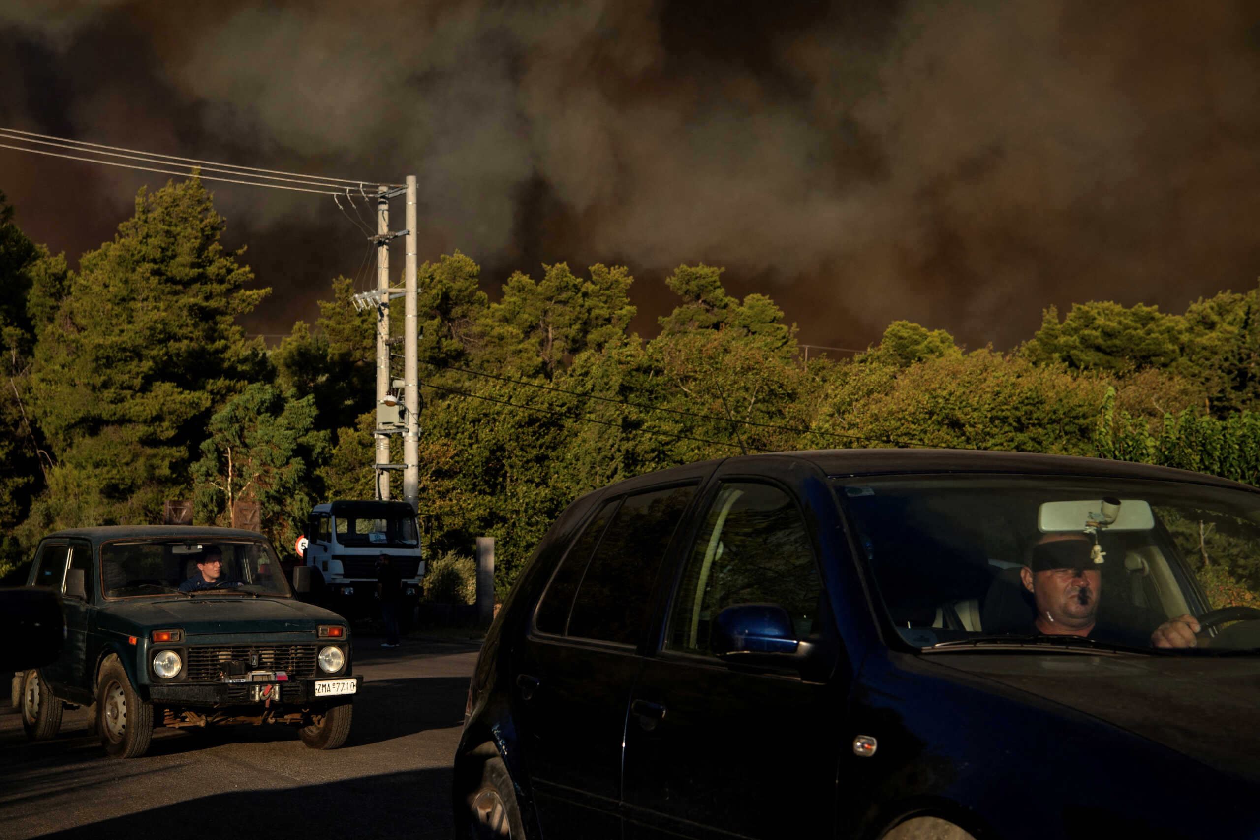 People drive as smoke rises from a wildfire burning in the village of Varnavas, near Athens, Greece, August 11, 2024. REUTERS