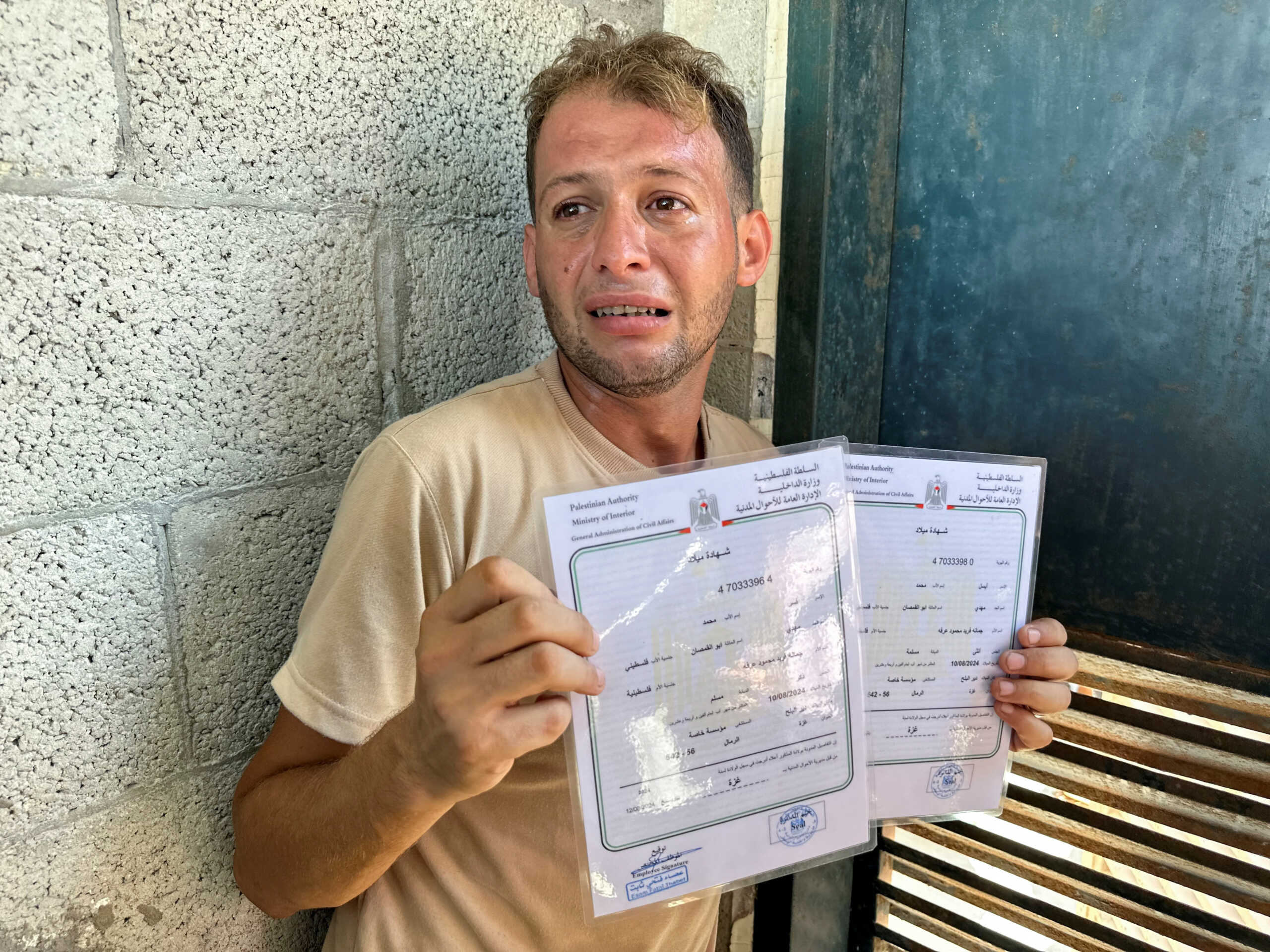 Mohammed Abu Al-Qumsan, whose wife Jumann, and newborn twins Asser and Ayssel were killed in an Israeli strike while he was brining the twins' birth of certificates, according to medics, reacts as he holds the certificates, in Deir Al-Balah in the central Gaza Strip, August 13, 2024. REUTERS