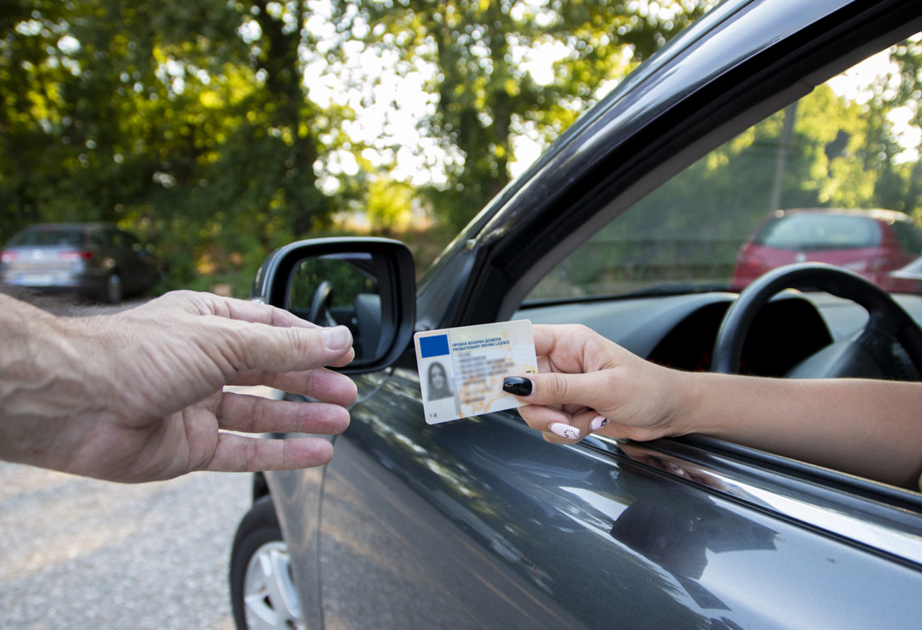 Teenager driver commited a minor offence and handing over her licence to a police officer reaching towards the open window.Police officer controlling traffic on the road