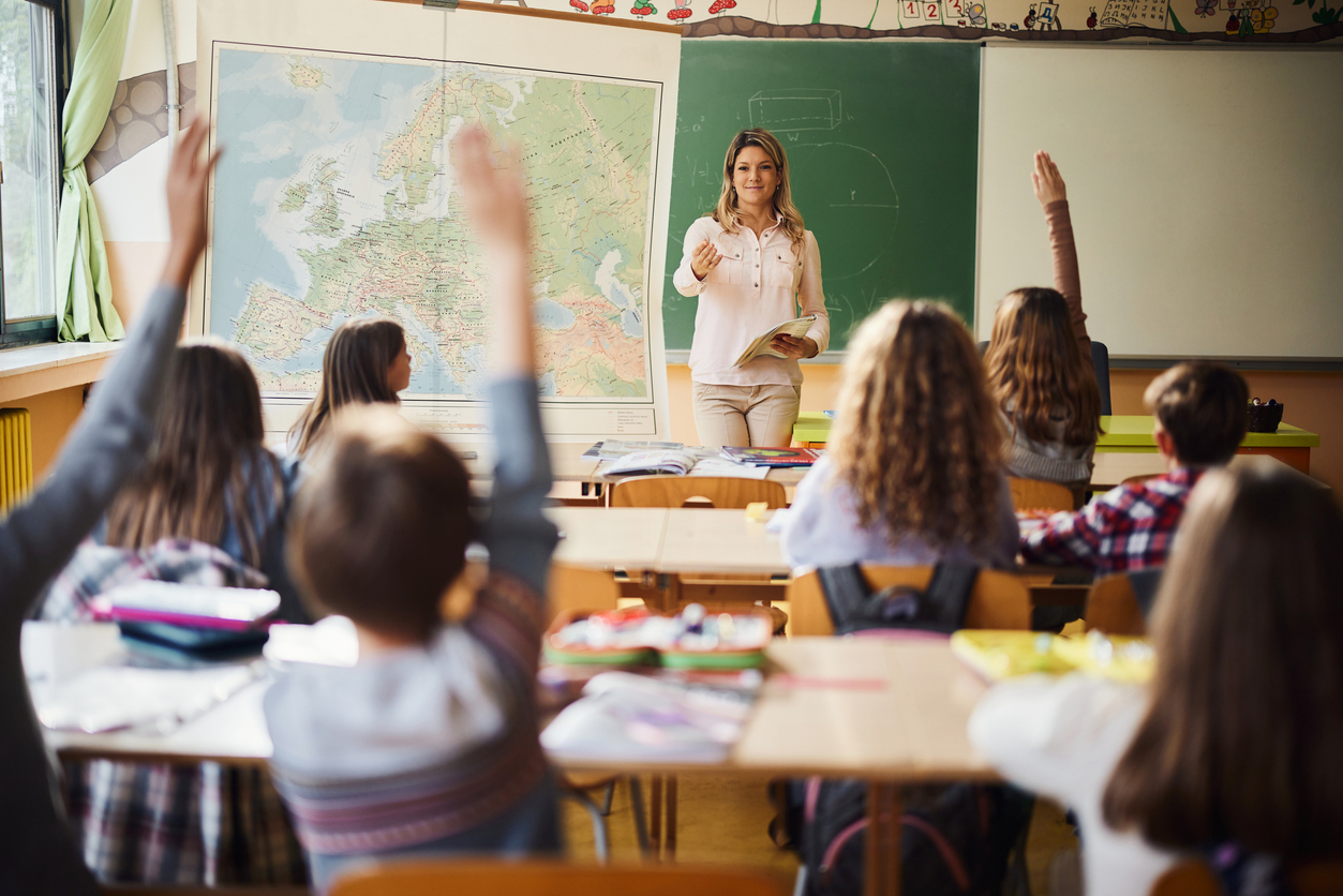 Smiling teacher aiming at her elementary students while wanting to hear the answers to her question.