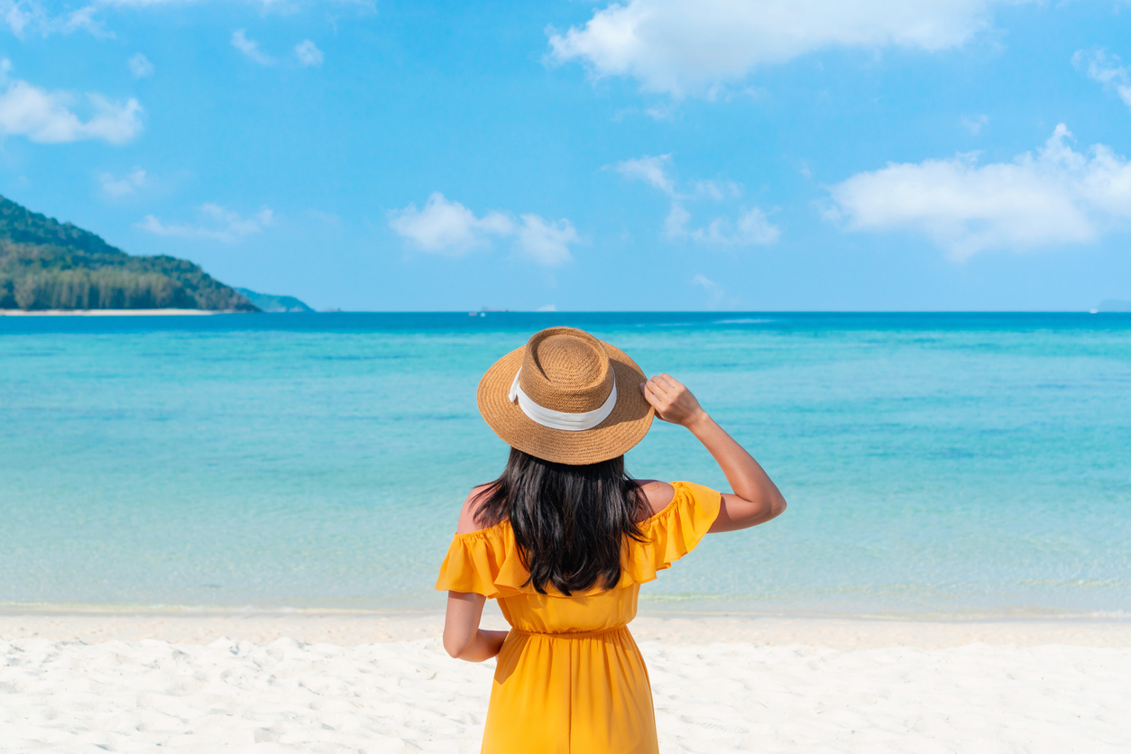 Happy traveler Asian woman on yellow dress relax on the tropical sandy beach. Summer, holiday concept. Copy space