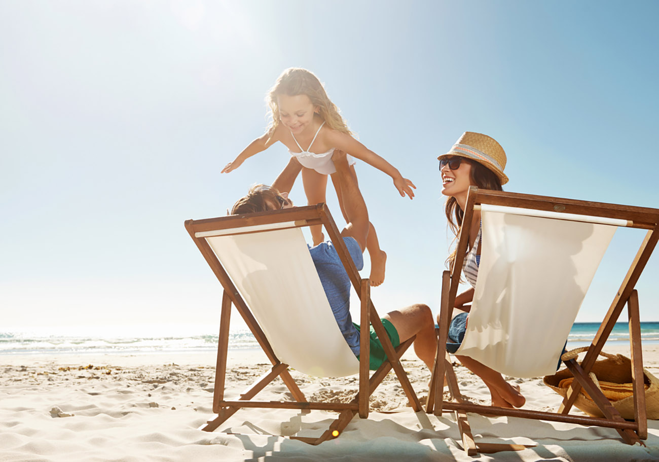Shot of a man sitting on the beach with his family while lifting his daugther to the skyhttp: