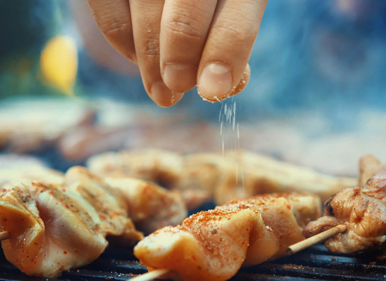 Closeup of unrecognizable male chef seasoning meat on a grill with a pinch of salt. Very shallow focus.