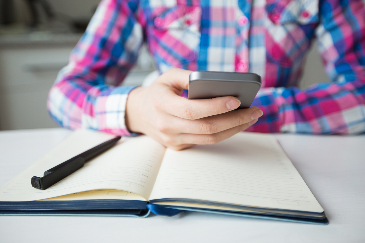 Cropped view of person hands texting on smartphone and diary