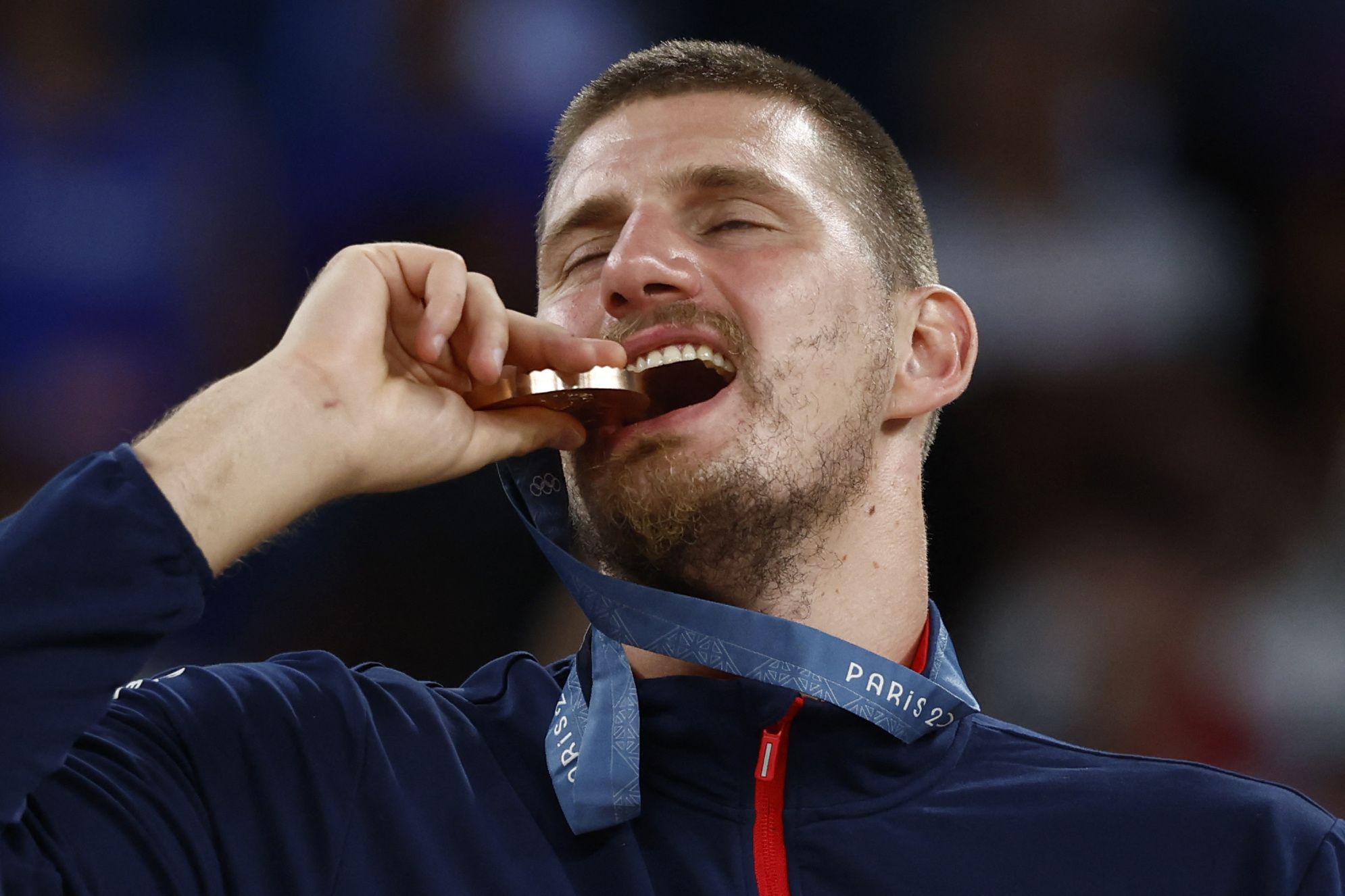 Paris 2024 Olympics - Basketball - Men's Victory Ceremony - Bercy Arena, Paris, France - August 10, 2024. Bronze medallist Nikola Jokic of Serbia bites his medal. REUTERS