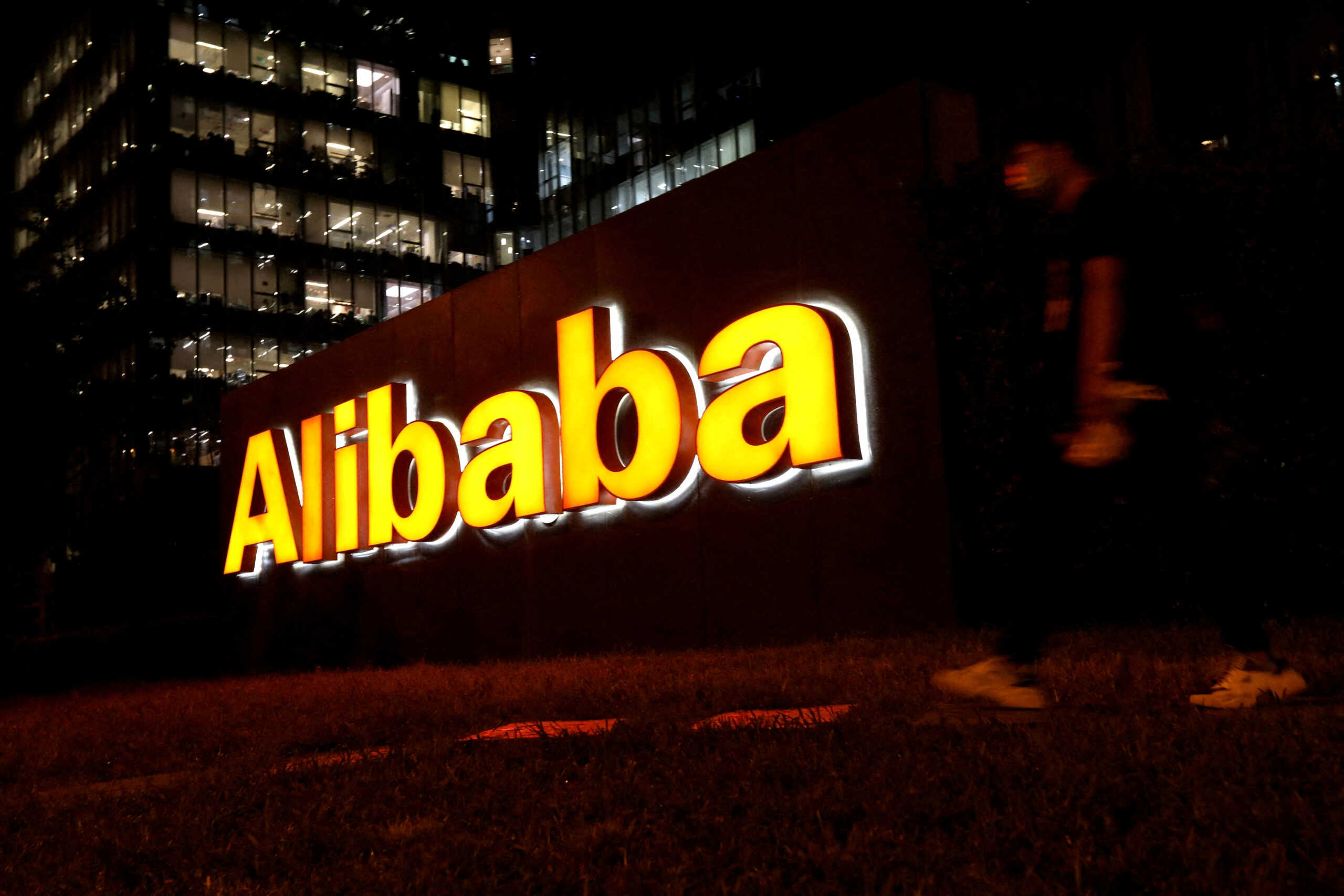 FILE PHOTO: A man walks past a logo of Alibaba Group at its office building in Beijing, China August 9, 2021. REUTERS