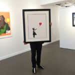 epaselect epa09152365 A gallery employee poses with an artwork by British artist, Banksy 'Girl with a baloon' at the 'Millennials' exhibition at the Hofa gallery in London London, Britain, 22 April 2021. The new exhibition features artists such as Banksy, Nina Chanel Abney, Jonas Wood, Josh Sperling, Yoshimoto Nara and will open to the public on 23 April.  EPA