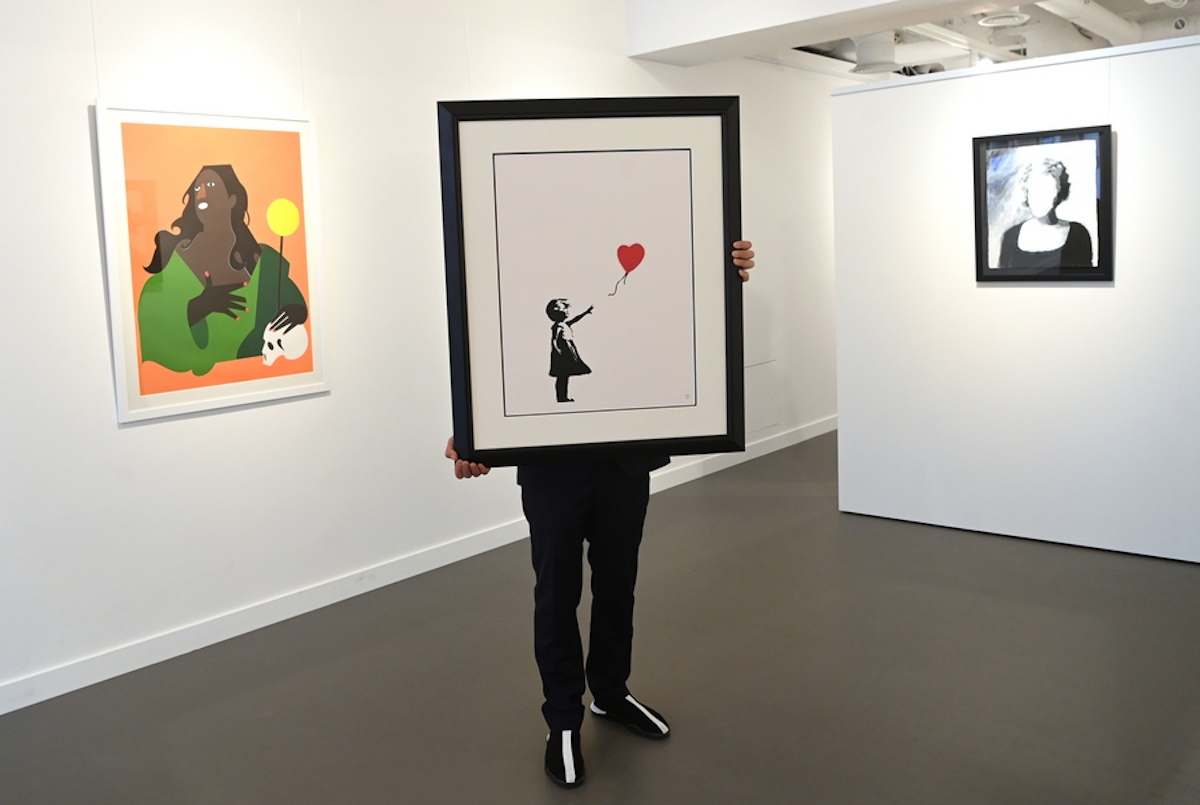 epaselect epa09152365 A gallery employee poses with an artwork by British artist, Banksy 'Girl with a baloon' at the 'Millennials' exhibition at the Hofa gallery in London London, Britain, 22 April 2021. The new exhibition features artists such as Banksy, Nina Chanel Abney, Jonas Wood, Josh Sperling, Yoshimoto Nara and will open to the public on 23 April.  EPA