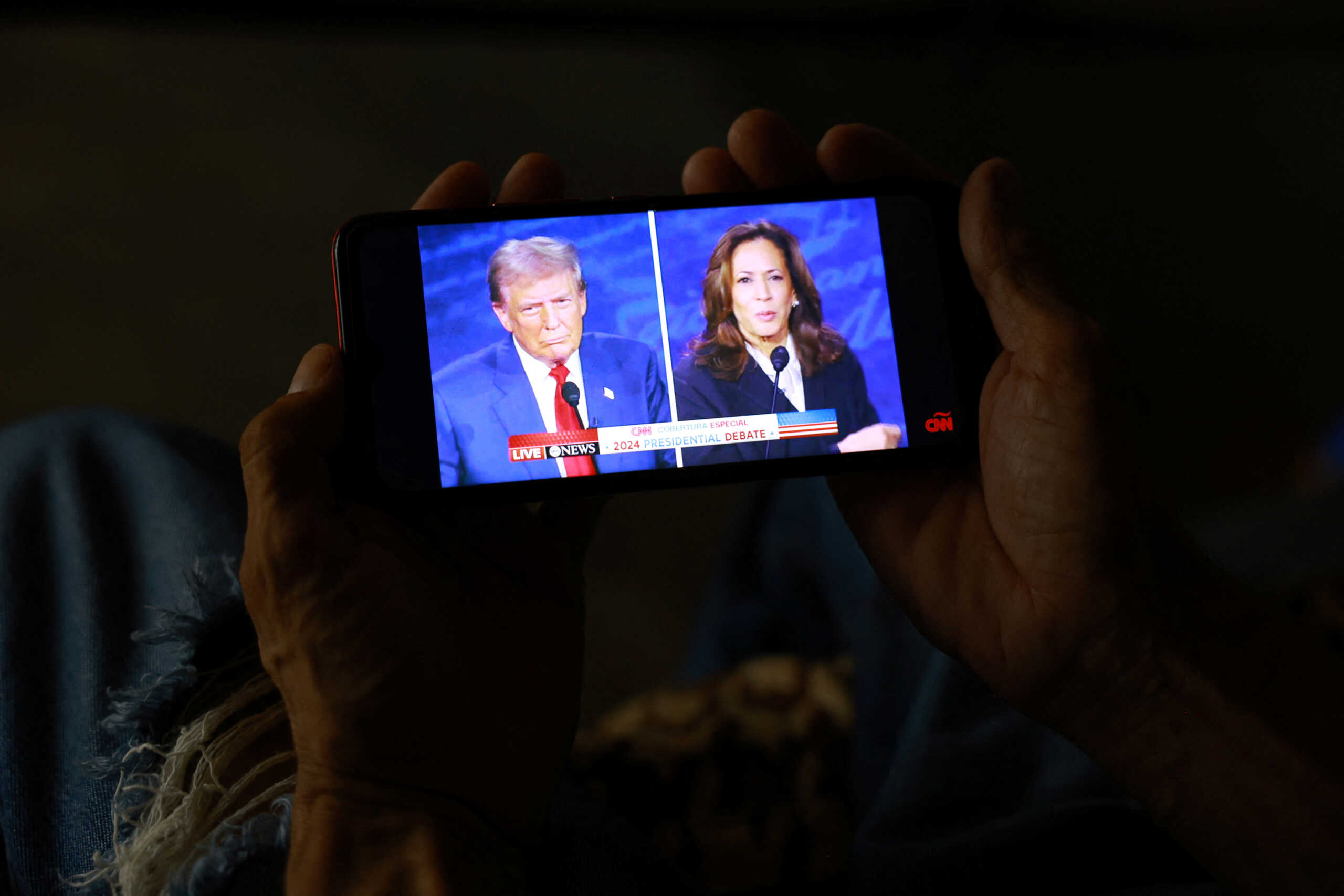 A migrant, seeking to reach the United States and request asylum, watches the presidential debate between the Republican presidential nominee, former U.S. President Donald Trump and the Democratic presidential nominee, U.S. Vice President Kamala Harris, on a mobile phone screen inside the El Buen Samaritano shelter in Ciudad Juarez, Mexico, September 10, 2024. REUTERS