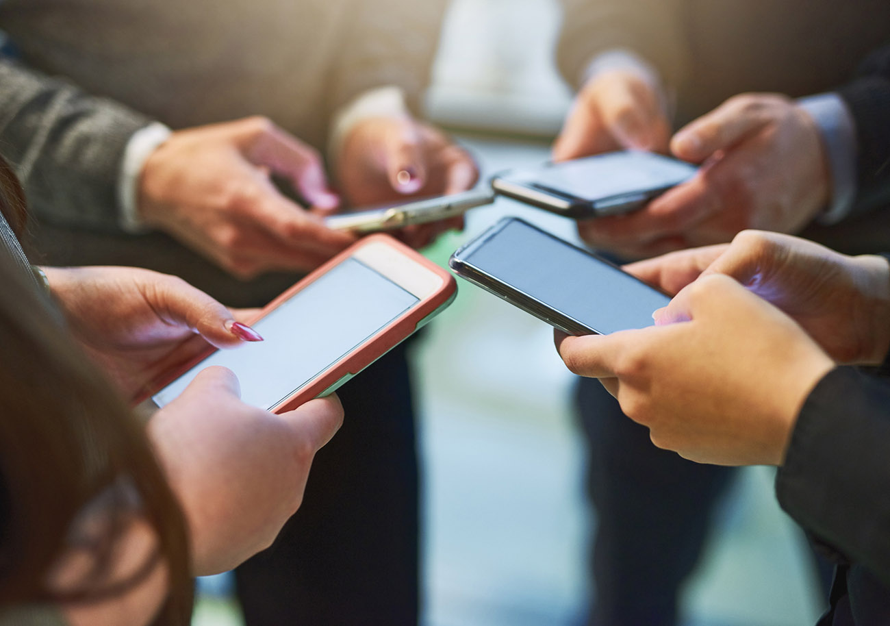Cropped shot of a group of unrecognizable businesspeople huddled together using cellphones in an office