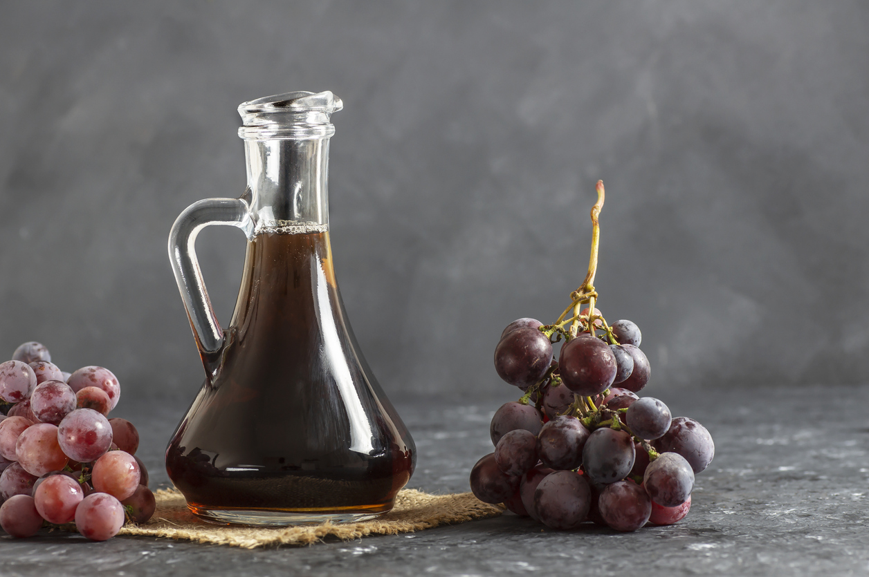 Glass bottle of organic black grape balsamic vinegar made from fermented fresh grapes. Healthy organic food black fruit, selective focus