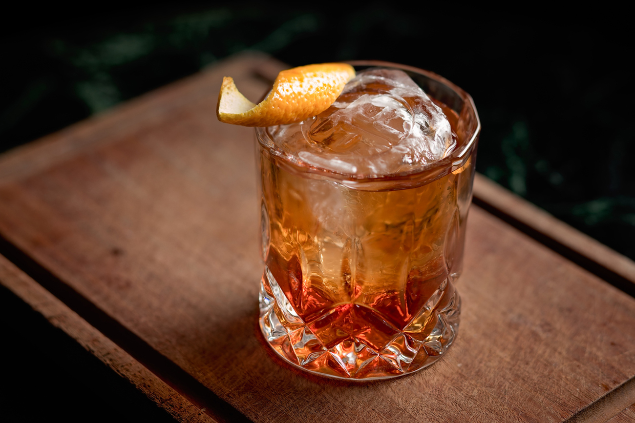 Old fashioned cocktail with an orange twist, an ice ball, present over a wooden board