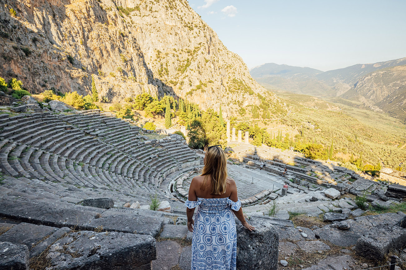 Rear view of female tourist exploring old ruins of Greek Amphitheatre against mountains during sunny day