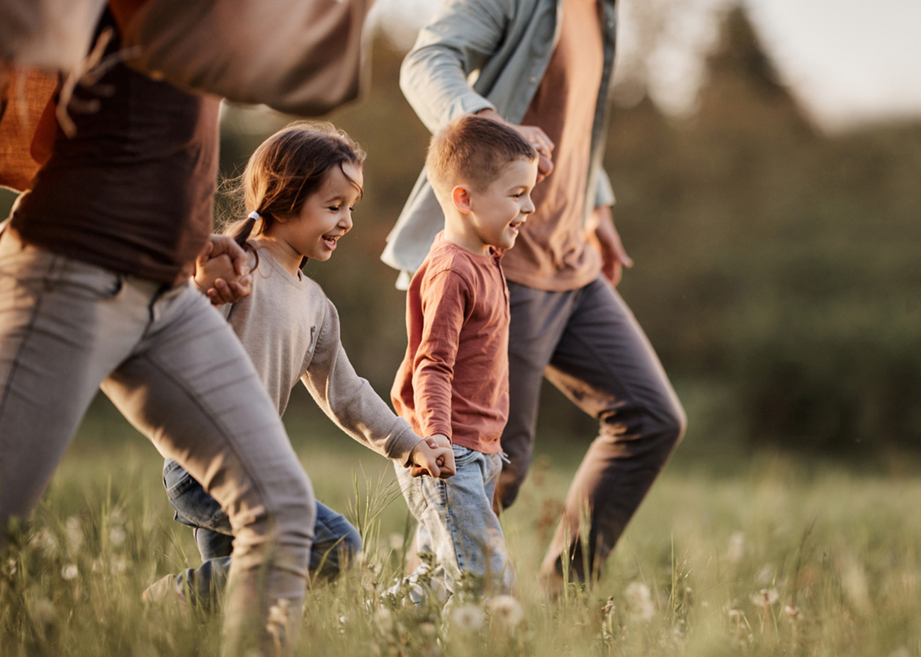 Happy siblings having fun while holding hands with their parents and running during spring day in nature. Copy space.