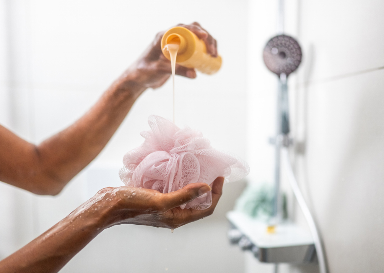 Woman pouring shower gel on bath sponge while taking shower close up