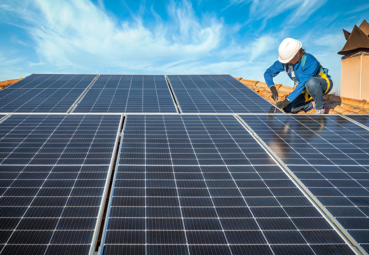 Female engineer in blue suit and protective helmet installing photovoltaic panel system. Professional electrician mounting solar module on roof. Alternative energy ecological concept