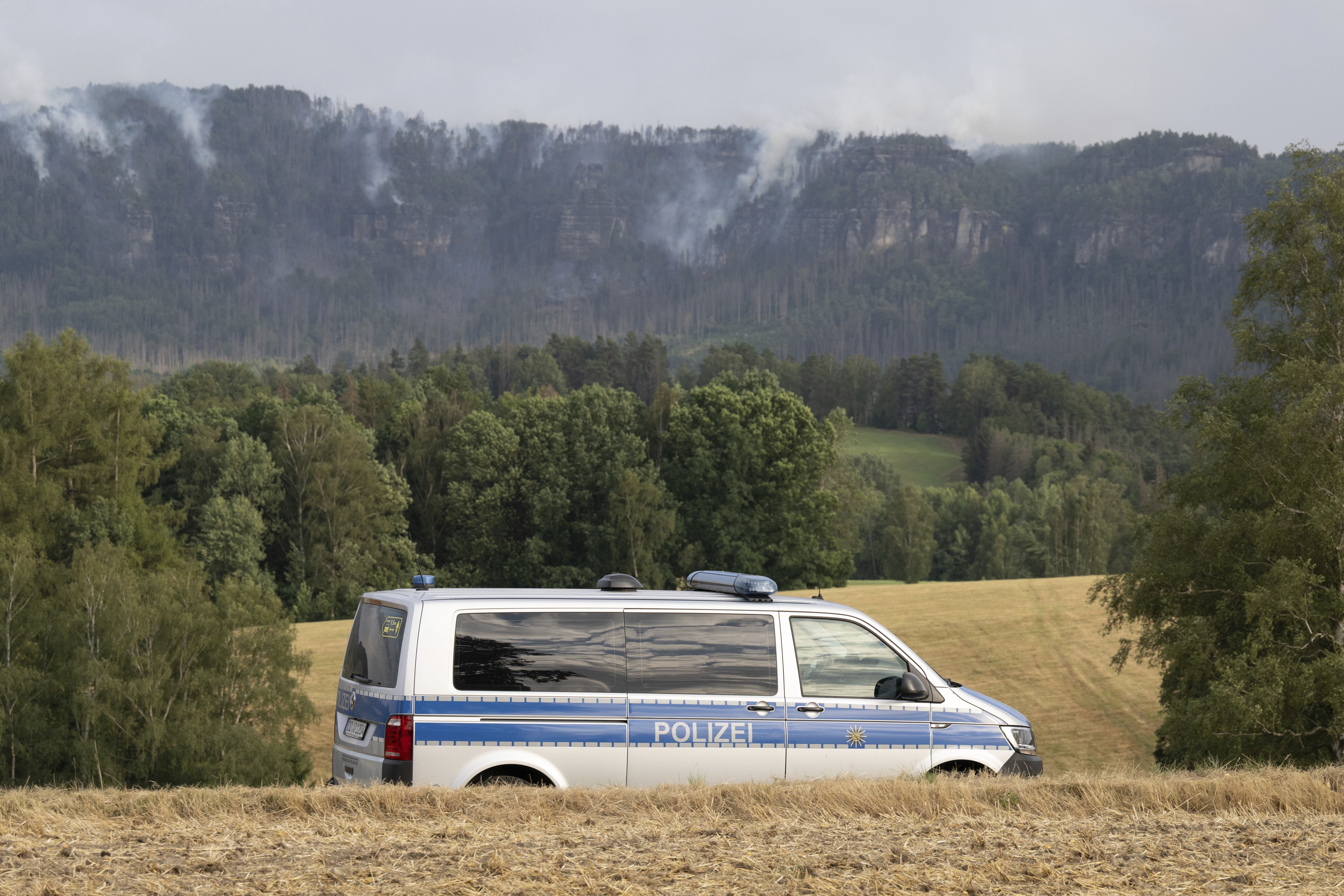 26 July 2022, Saxony, Lichtenhain: A police car drives along a road in front of a fire in the Saxon Switzerland National Park. The situation in the forest fire in the Saxon Switzerland National Park has worsened. Photo by: Sebastian Kahnert