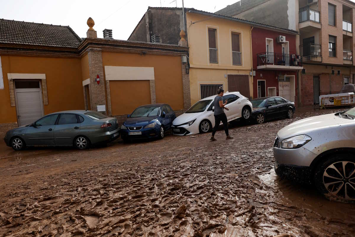 A person walks next to damaged cars along a mud-covered street after torrential rains caused flooding in Guadassuar, Valencia region, Spain, October 30, 2024. REUTERS