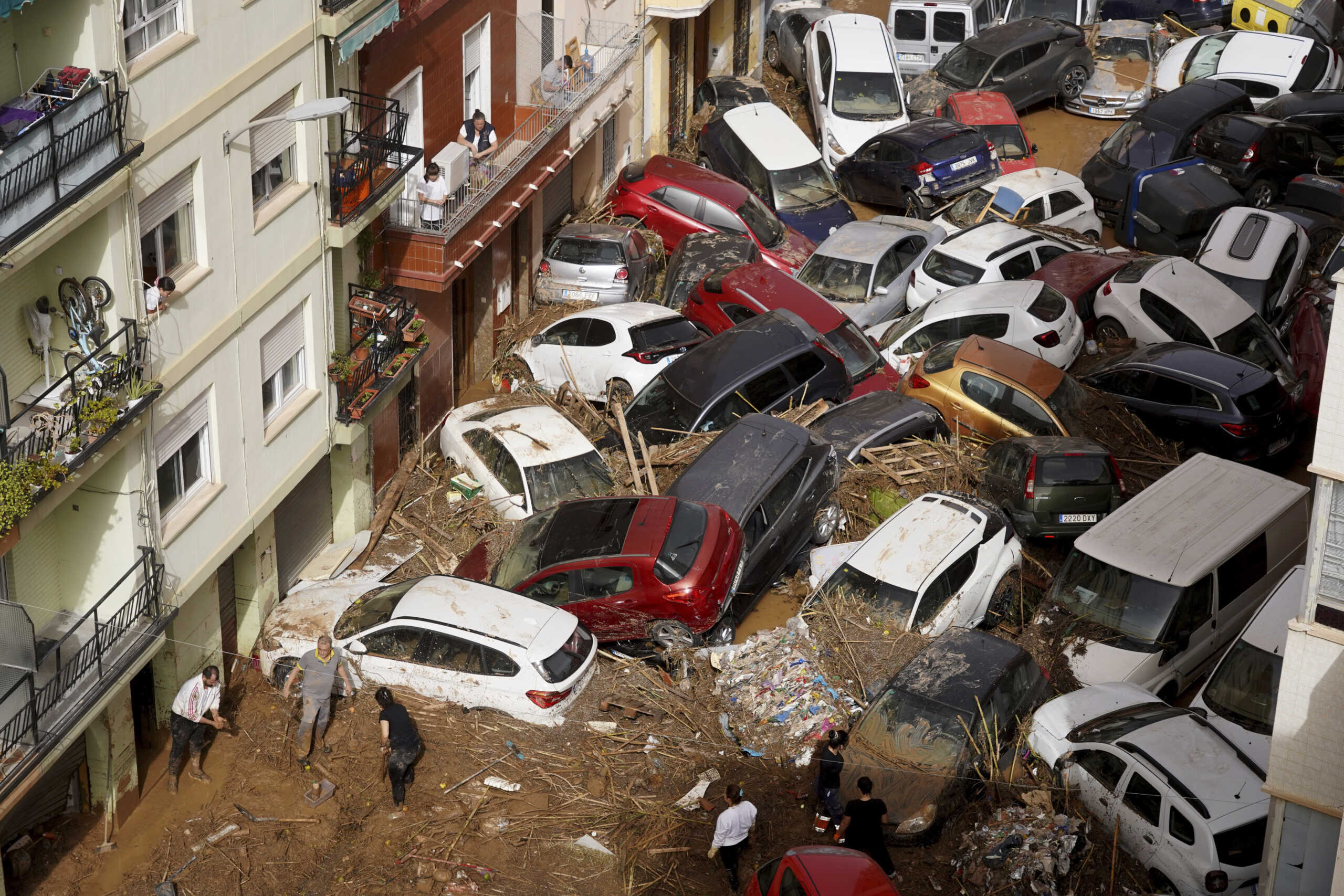 Residents clean the street next to cars piled up after being swept away by floods in Valencia, Spain, Wednesday, Oct. 30, 2024. (AP Photo