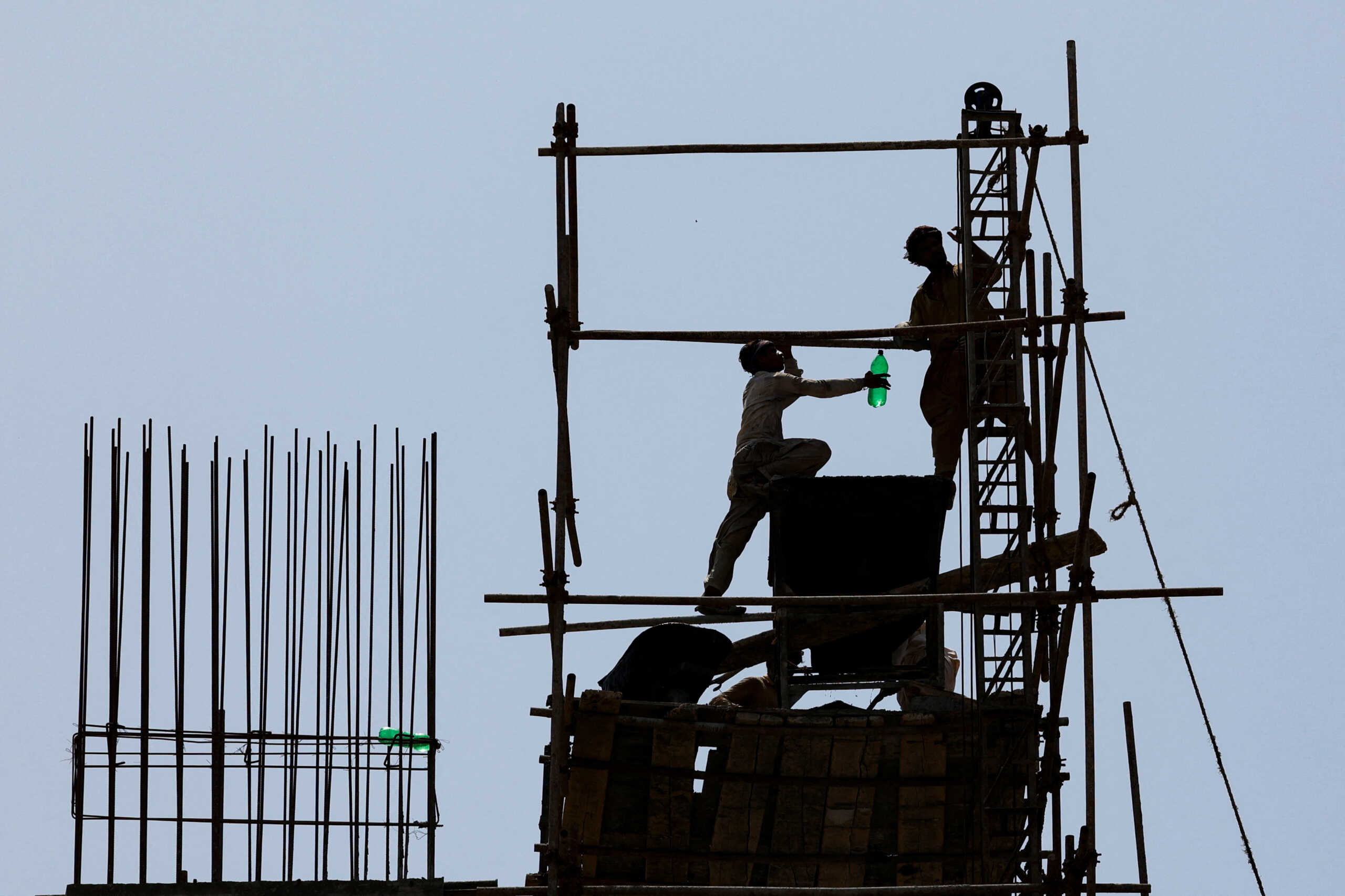 Labourers are silhouetted as they stand on scaffoldings at a construction site during a hot and humid day in Karachi, Pakistan May 20, 2024. REUTERS