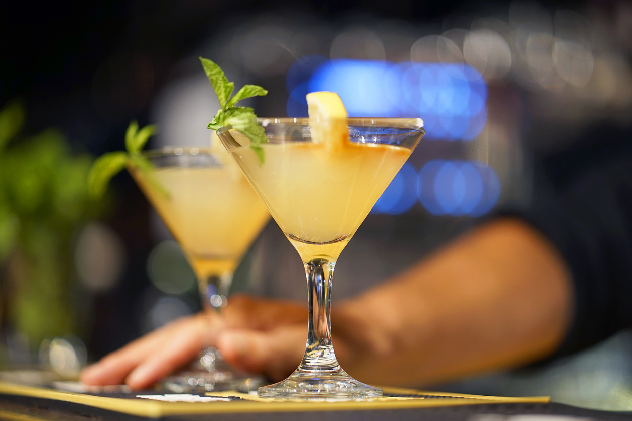 The barman gives a cocktail to the client of the hotel bar. Fresh cocktail with orange. Alcoholic, non-alcoholic drink-beverage at the bar counter in the night club. Glass of lemon cocktail.