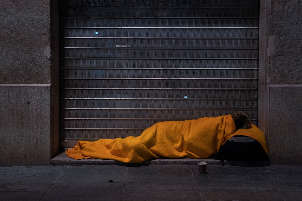 A homeless person sleeps on the street under a blanket in front of a storefront during the second covid pandemic containment, Lyon, France, 2020