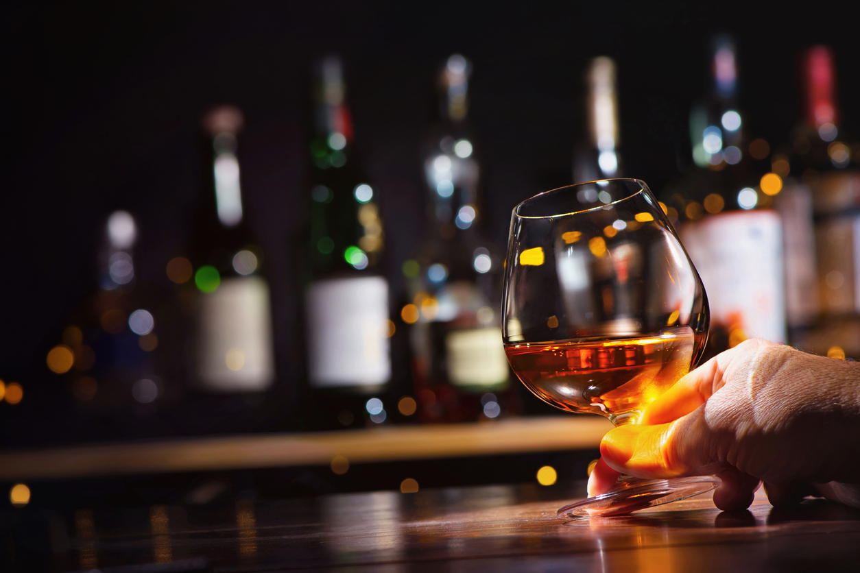 Male hand with glass of whiskey or brandy on bar counter