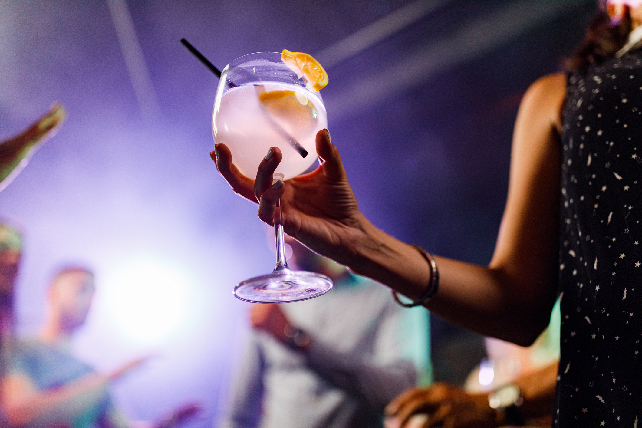 Close up of unrecognizable woman with a cocktail during disco dancing in a bar.