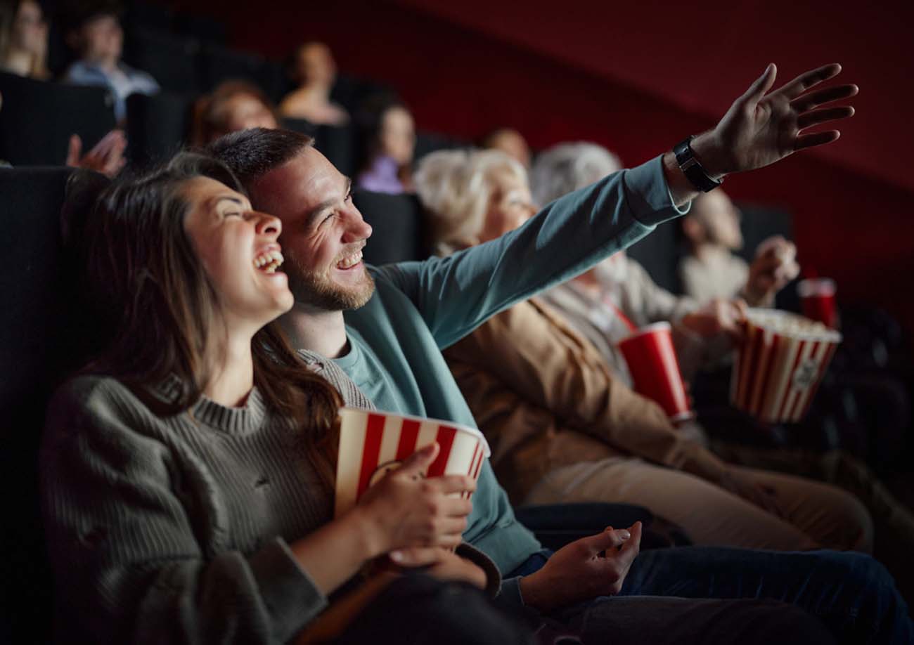 Cheerful couple having fun while laughing during a comedy movie in cinema. Focus is on man.
