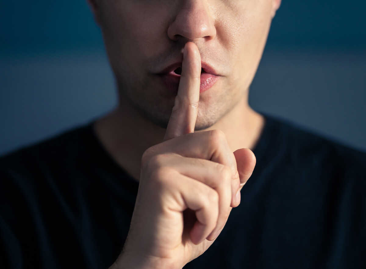 Secret and silence. Quiet silent shh gesture with finger on lips. Man doing expression with hand on mouth. Taboo topic, censorship or freedom or speech. Conspiracy theory. Confidential talk.
