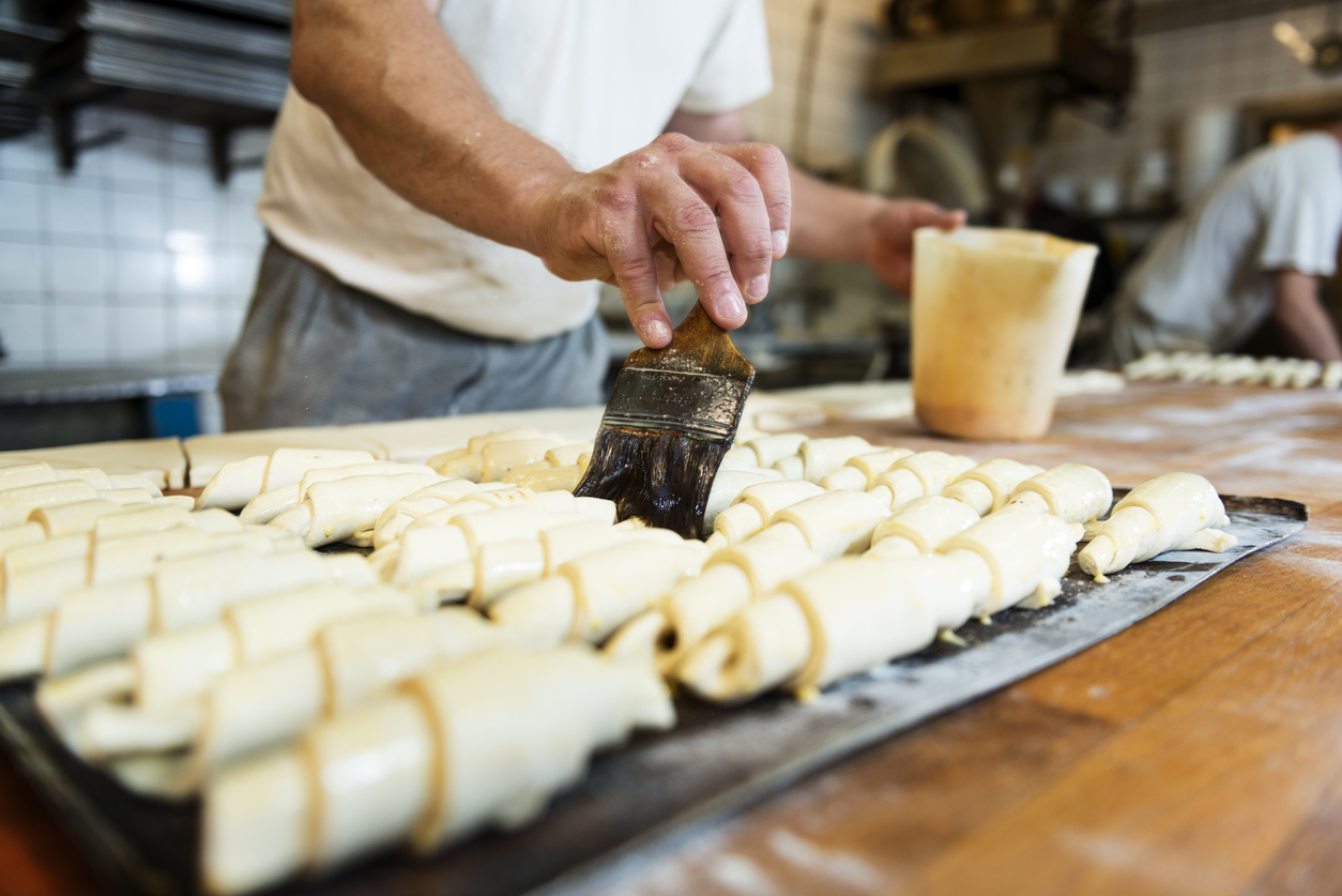 Baker brushing butter over some freshly made croissants. Photographed in a traditional bakery in Denmark.