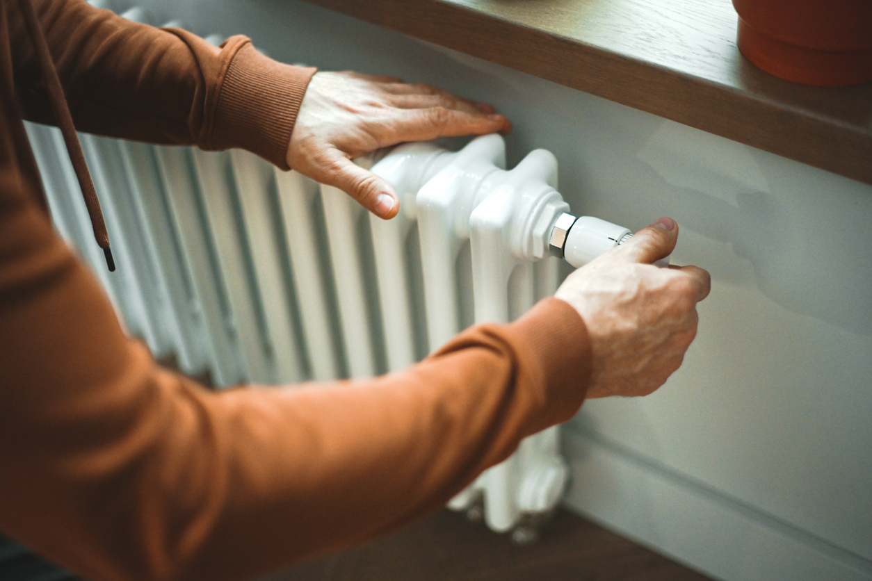 Mature adult man warms himself by the radiator in the room