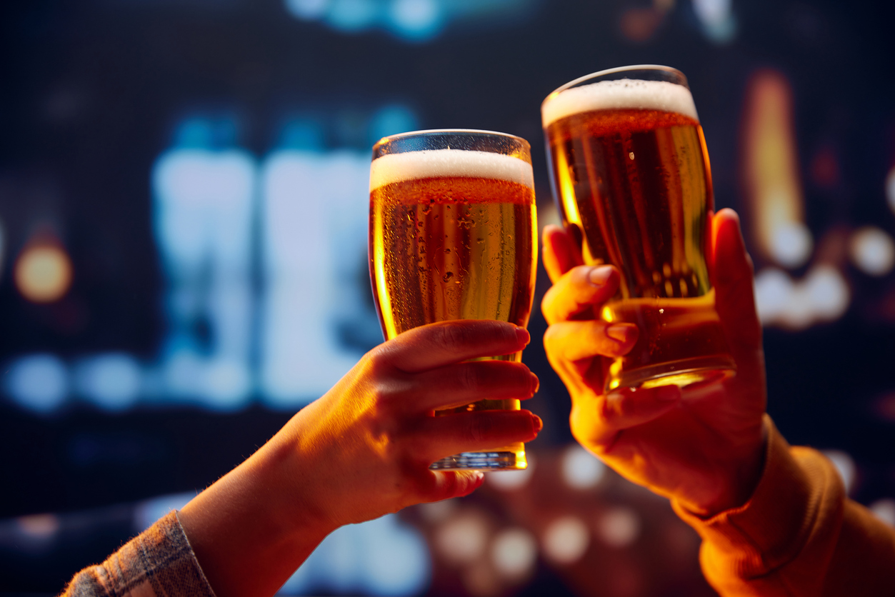 Hands holding lager light foamy big beer glasses and clinking. Two friends sitting in bar and drinking alcohol drinks. Concept of Beer  Fest, party, celebration, taste, national traditions.