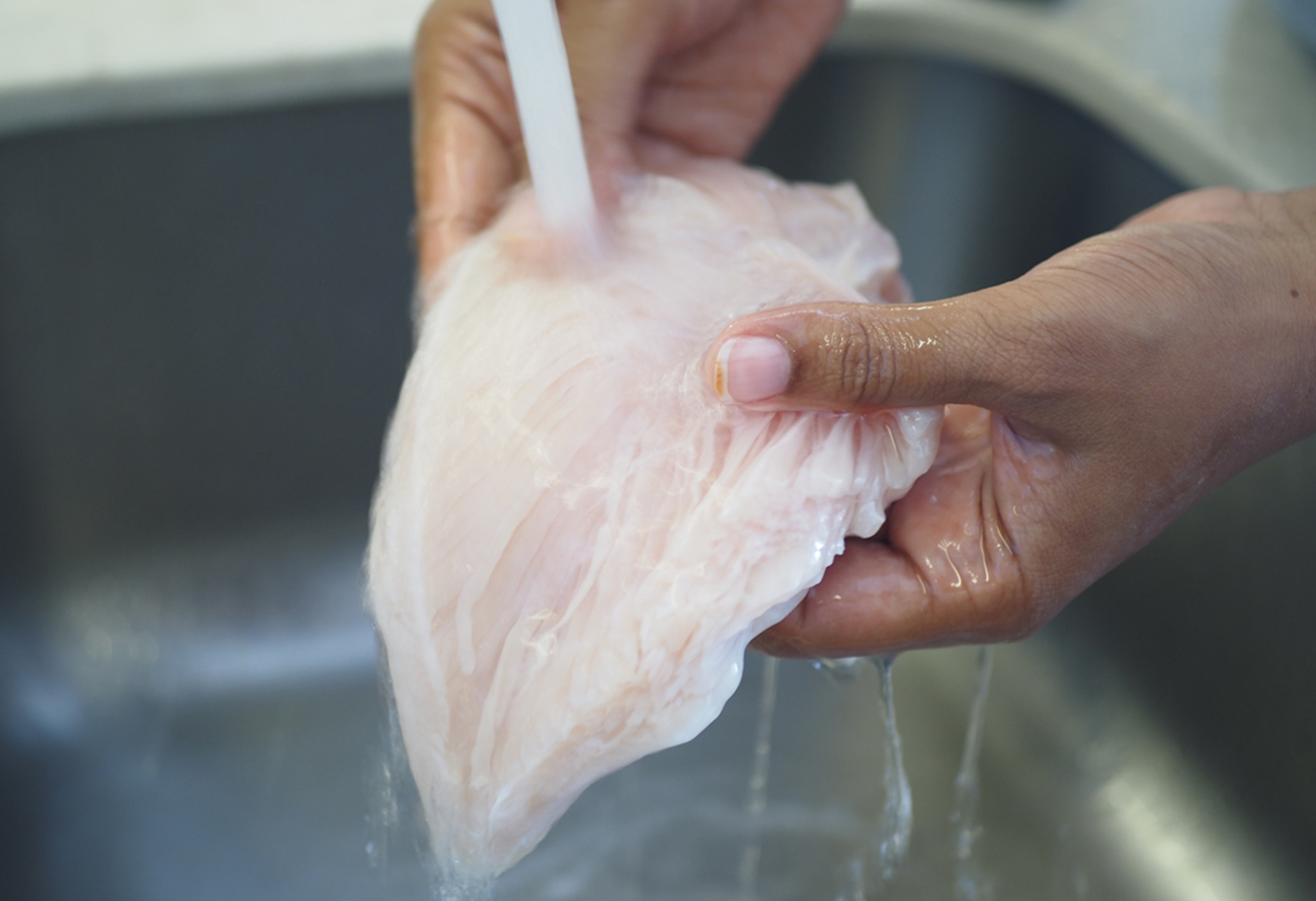 Female hands washing and cleaning chicken breast