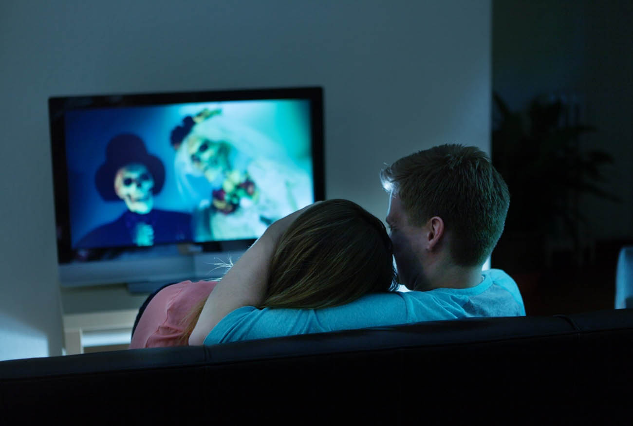 Couple watching Scary Halloween horror movie on TV together at home.