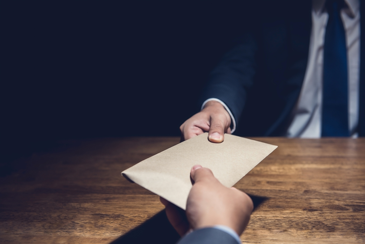 A man giving bribe money in a brown envelope to another businessman in a corruption scam