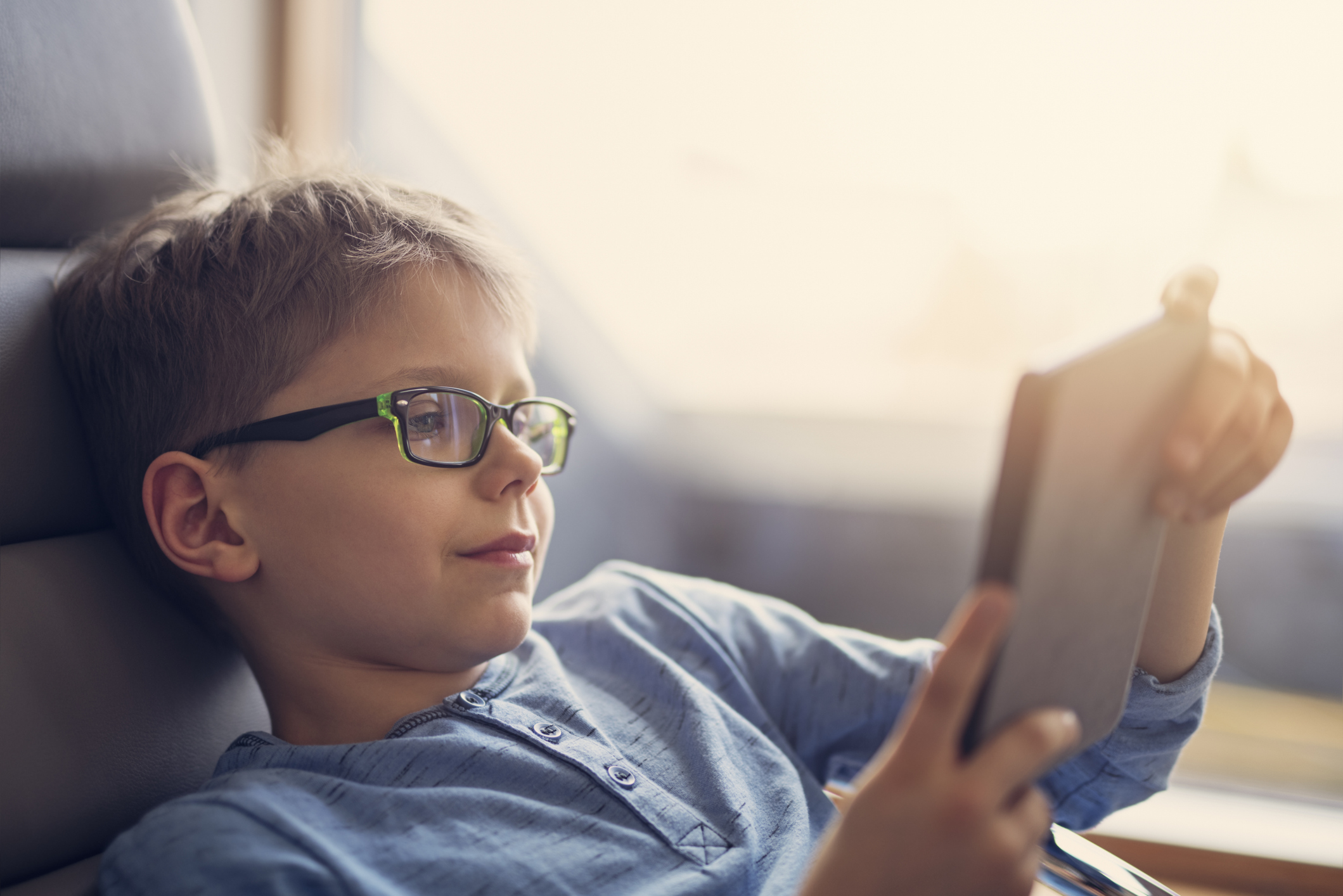 Happy boy aged 8 reading an e-book using e-reader. The boy is sitting comfortably in armchair, Sunny day.
Nikon D850