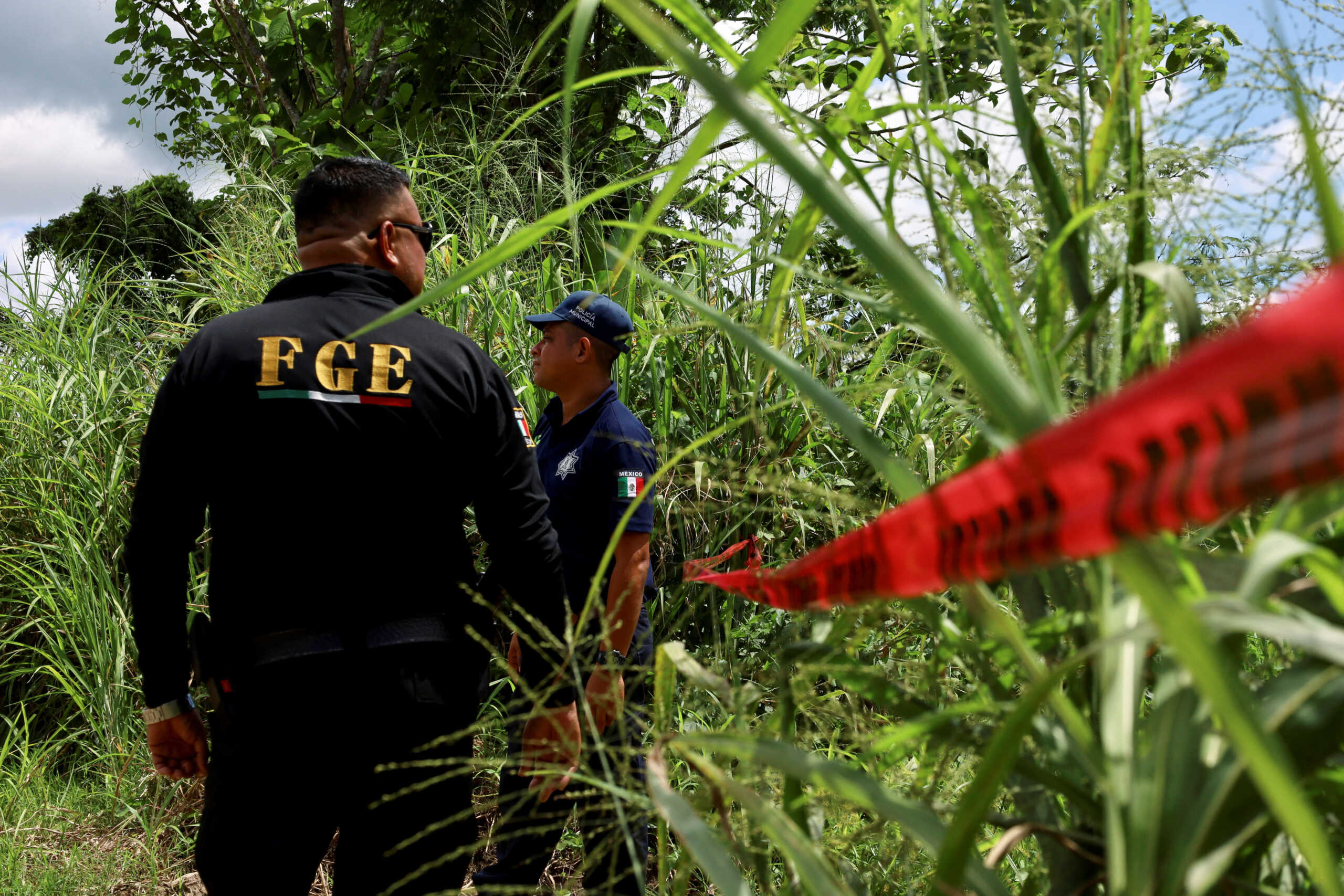 Members of Mexico's Prosecutor's General Office stand near police tape at a crime scene where two dead migrants were found half-buried in the ground, near Mexico's southern border with Guatemala, in Huixtla, Mexico October 7, 2024. REUTERS
