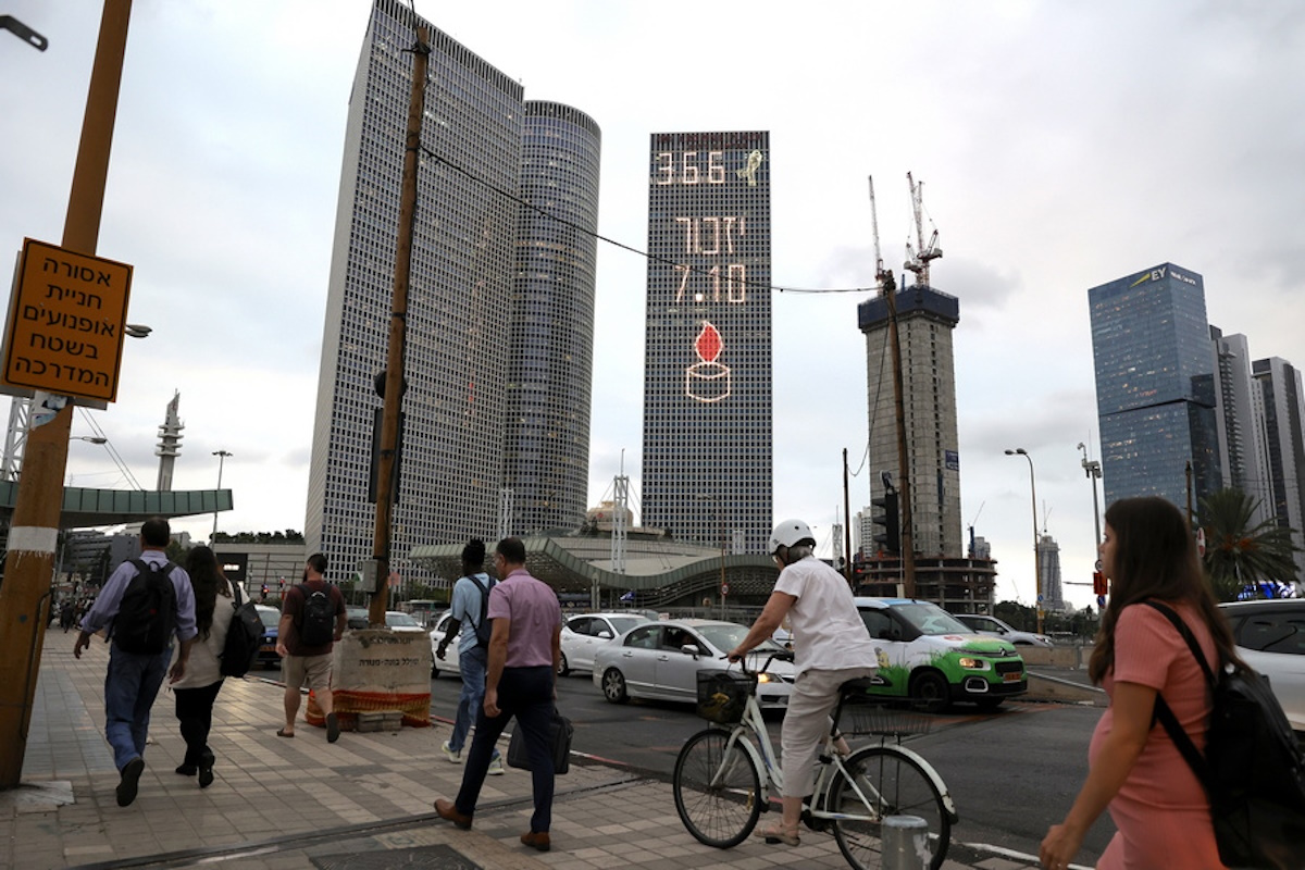 epa11646042 People pass by the Azrieli Center as Hebrew letters 'Yizkor 7.10', a memorial prayer for the departed meaning 'Remember', light one of its skyscrapers, in Tel Aviv, Israel, 06 October 2024. Upcoming 07 October 2024 marks one year since the Palestinian militant group Hamas launched a surprise attack on Israel, killing 1,200, and one year since Israel began its war on Gaza, killing more than 41,000 and destroying the Palestinian enclave.  EPA