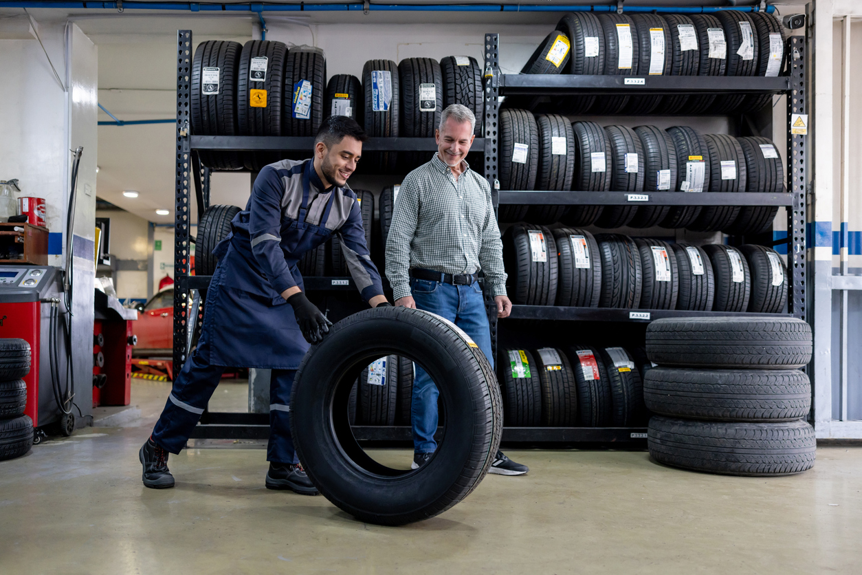 Latin American mechanic changing a car tire and talking to his client at the repair garage